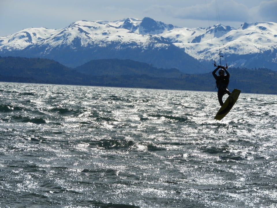 Kitesurfista saltando sobre el lago frente a montañas nevadas