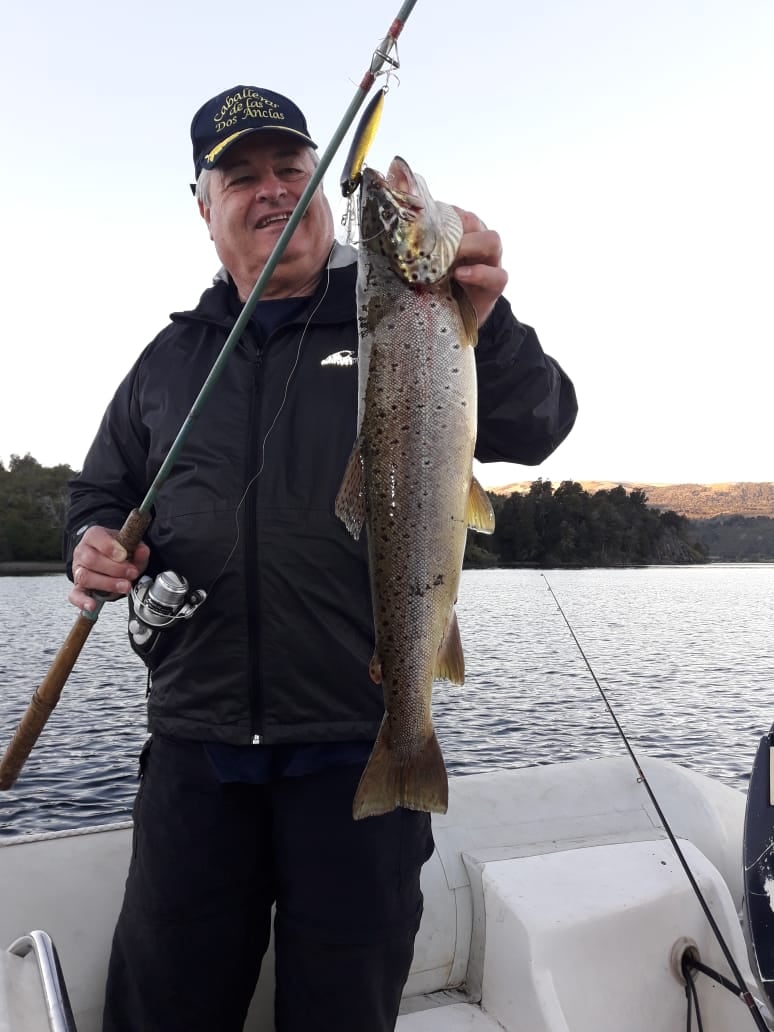 Pescador mostrando una trucha junto a su caña
