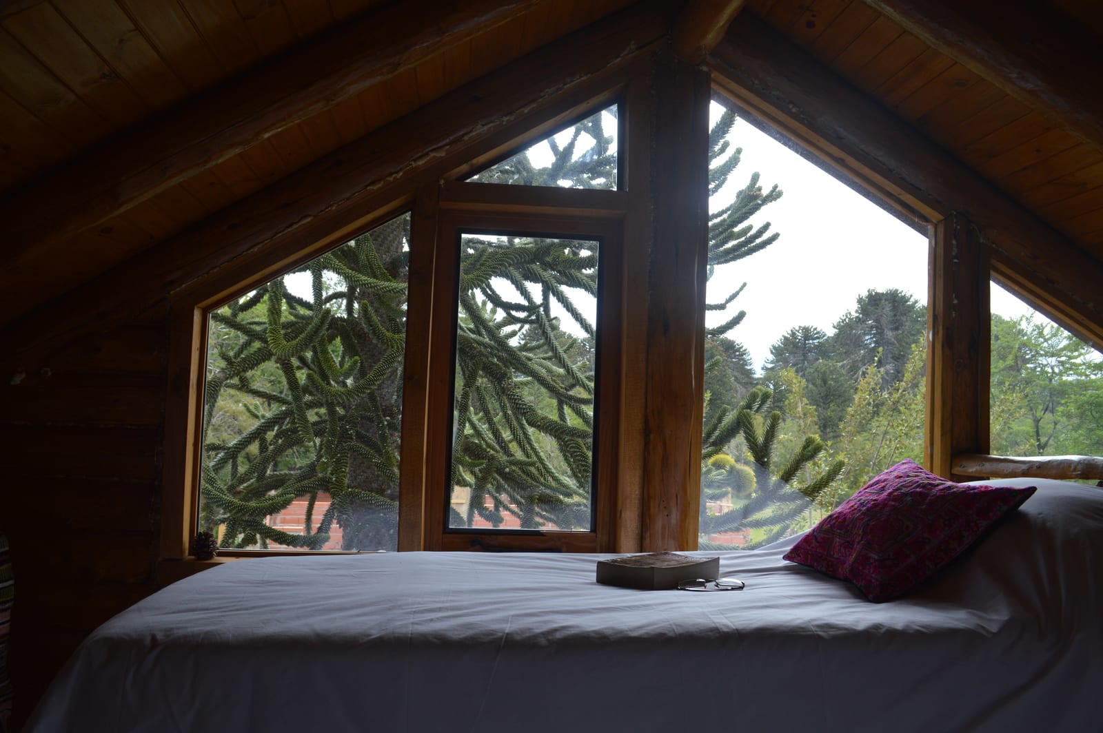 Cama en el altillo frente a un ventanal triangular.
