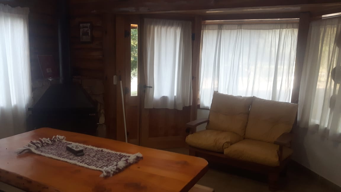 Estar con sillón mostaza, mesa y hogar a leña.