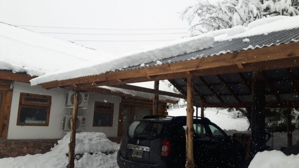Automóvil bajo una cochera de madera con nieve sobre el techo