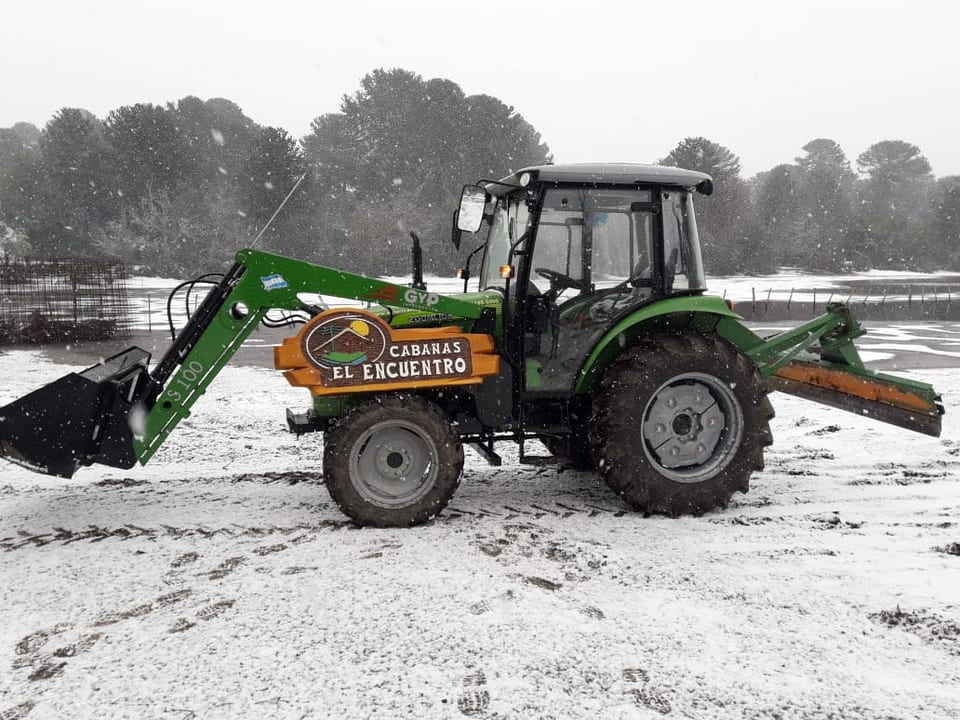 Tractor verde con pala y cartel de Cabañas El Encuentro sobre la nieve